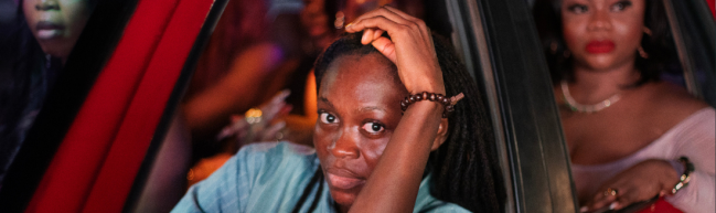 Lady sitzt in ihrem roten Taxi. In das offene Fenster gelehnt blickt sie hinaus und uns an.